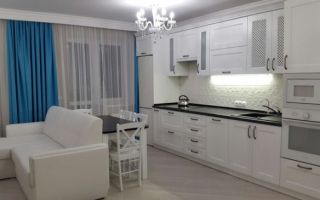 Интерьер белой кухни-гостиной 20 м<sup>2</sup> с черной столешницей и бирюзовыми шторами